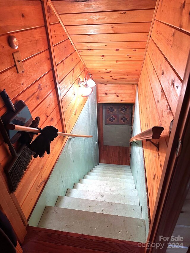 stairs featuring vaulted ceiling, wood walls, hardwood / wood-style floors, and wooden ceiling