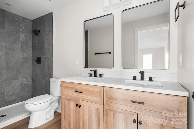 bathroom with toilet, vanity, hardwood / wood-style flooring, and a tile shower