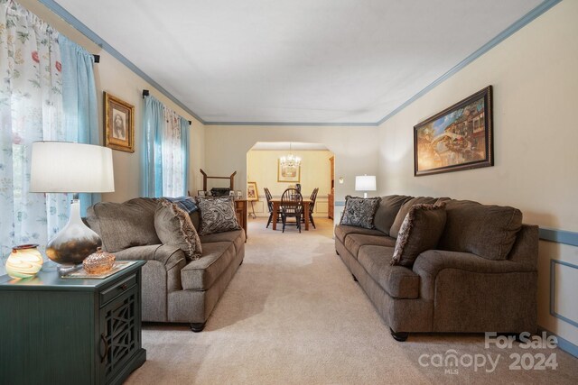 carpeted living room with crown molding and an inviting chandelier