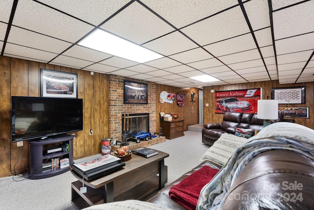 carpeted living room featuring a paneled ceiling, a brick fireplace, and wooden walls