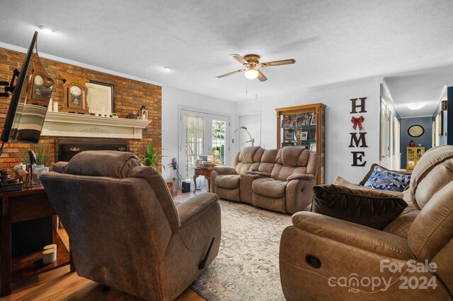 living room with a textured ceiling, brick wall, a fireplace, hardwood / wood-style floors, and ceiling fan