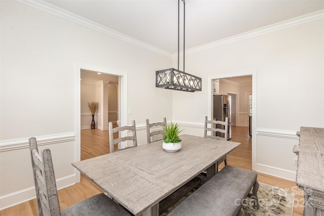 dining room with light wood-type flooring, crown molding, and baseboards