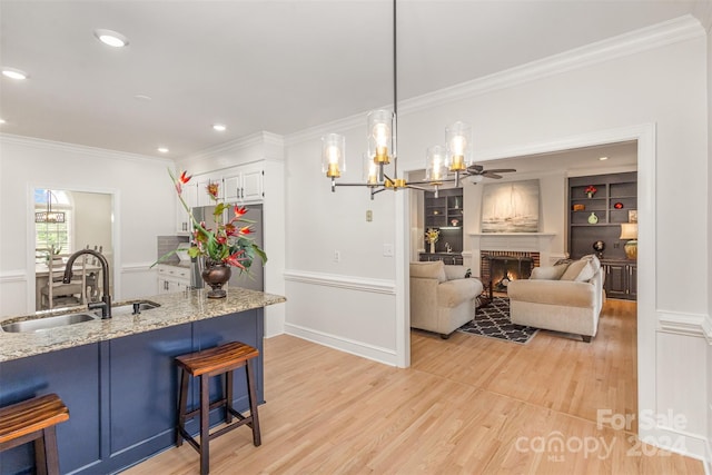 kitchen featuring light wood-style flooring, a breakfast bar area, light stone countertops, a brick fireplace, and a sink