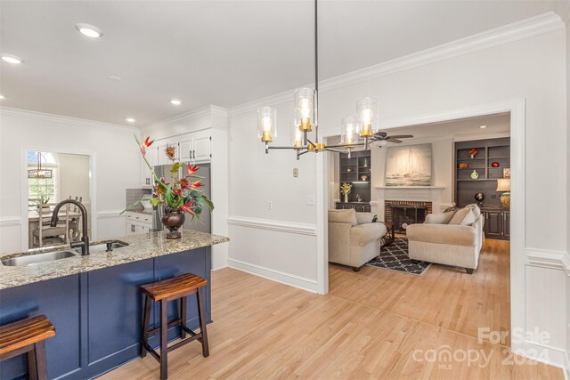 kitchen featuring a fireplace, a sink, light stone countertops, light wood finished floors, and a kitchen bar