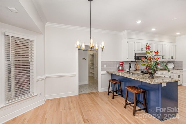 kitchen with light wood-type flooring, white cabinetry, stainless steel microwave, and a breakfast bar area