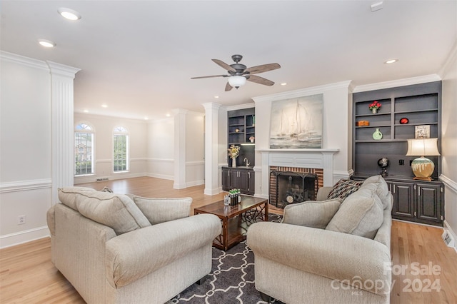 living room with decorative columns, light wood-style flooring, ornamental molding, a fireplace, and recessed lighting