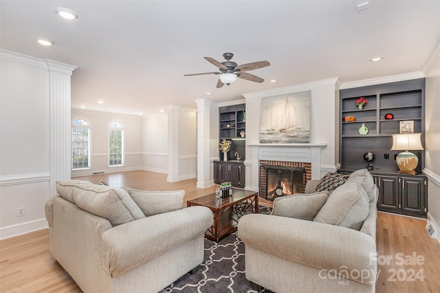 living area with light wood finished floors, recessed lighting, ornamental molding, a brick fireplace, and ornate columns