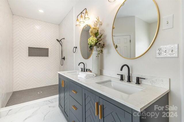 bathroom with double vanity, marble finish floor, a sink, and tiled shower