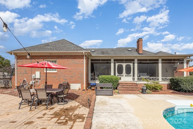 rear view of property with a sunroom, a patio area, a chimney, and brick siding