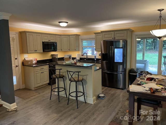 kitchen featuring hardwood / wood-style floors, a kitchen breakfast bar, black appliances, sink, and hanging light fixtures