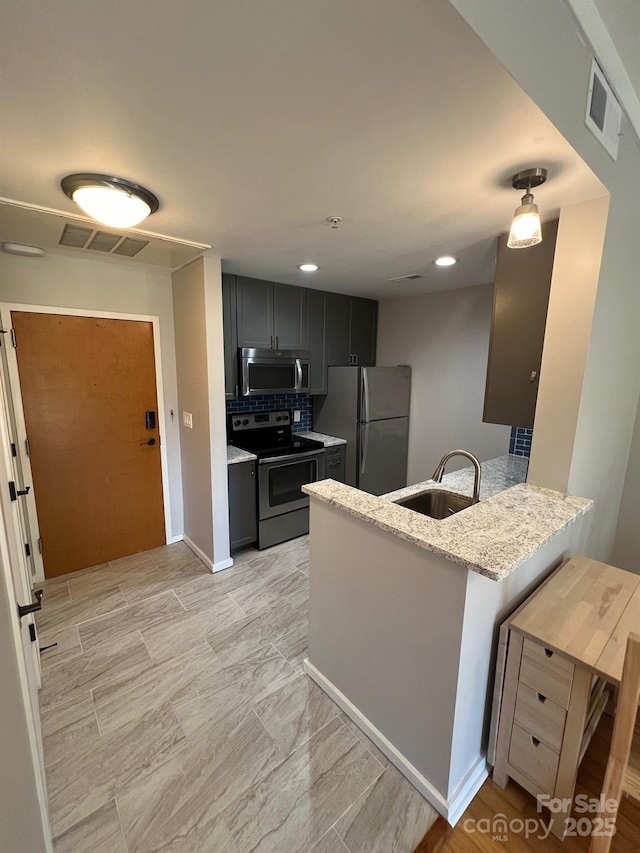 kitchen featuring appliances with stainless steel finishes, sink, decorative backsplash, light stone counters, and kitchen peninsula