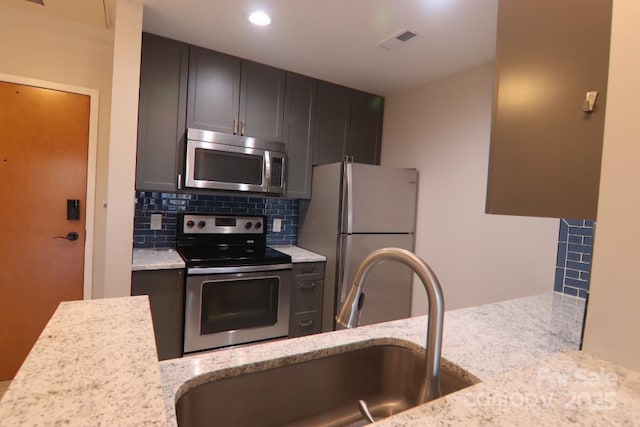 kitchen featuring sink, decorative backsplash, dark brown cabinetry, stainless steel appliances, and light stone countertops