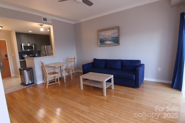 living room with ceiling fan, ornamental molding, and light wood-type flooring