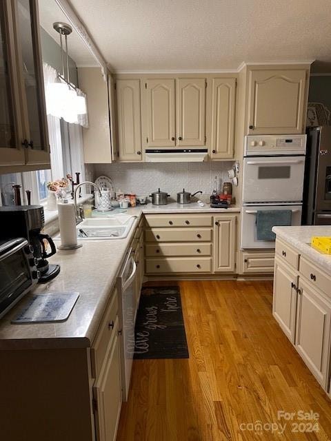 kitchen with double oven, hanging light fixtures, light hardwood / wood-style flooring, decorative backsplash, and black refrigerator with ice dispenser