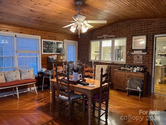 dining space with brick wall, vaulted ceiling, wood ceiling, hardwood / wood-style flooring, and ceiling fan