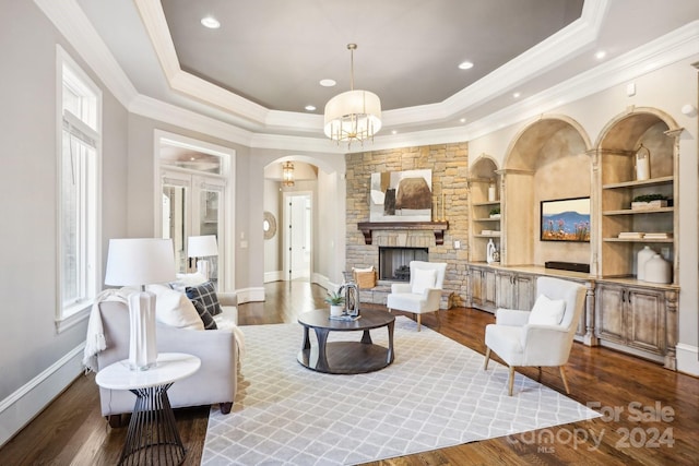 living room featuring a fireplace, a raised ceiling, dark wood-type flooring, crown molding, and a notable chandelier