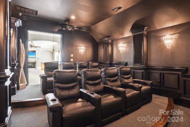 carpeted home theater room featuring lofted ceiling, ceiling fan, ornamental molding, ornate columns, and a fireplace