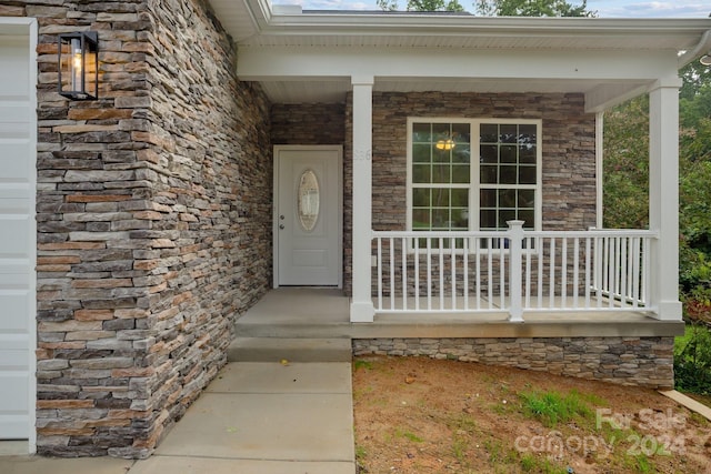 property entrance with covered porch, stone siding, and a garage