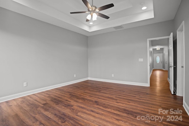 spare room featuring ceiling fan, dark wood-style flooring, visible vents, baseboards, and a raised ceiling