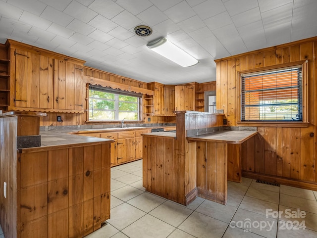 kitchen with kitchen peninsula, light tile patterned floors, sink, and wood walls