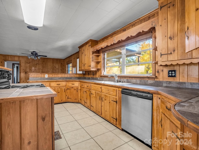 kitchen featuring stainless steel dishwasher, sink, tile countertops, range, and wood walls