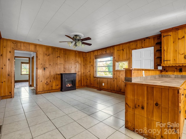 kitchen with wood walls, ceiling fan, light tile patterned floors, tile counters, and kitchen peninsula