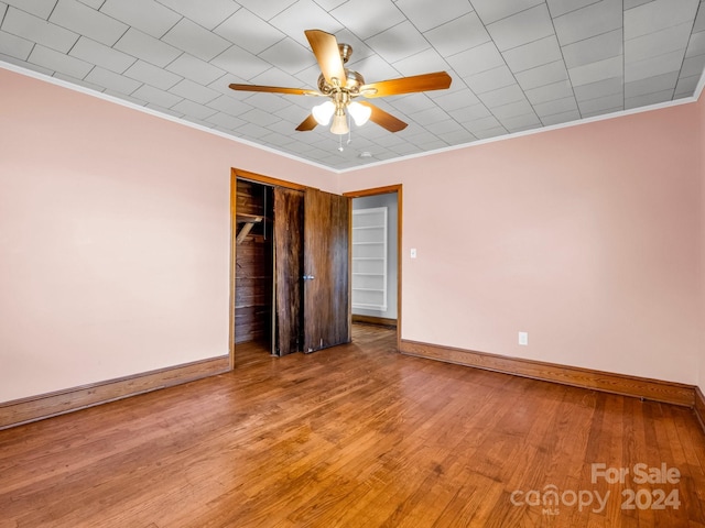 unfurnished bedroom featuring ceiling fan, a closet, ornamental molding, and hardwood / wood-style flooring