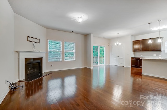 unfurnished living room featuring an inviting chandelier and dark wood-type flooring