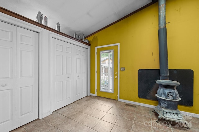 foyer featuring lofted ceiling, light tile patterned floors, and a wood stove