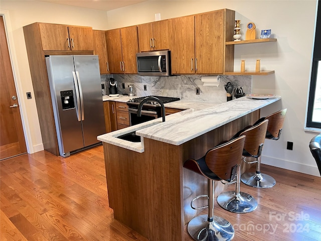 kitchen featuring stainless steel appliances, light hardwood / wood-style floors, kitchen peninsula, tasteful backsplash, and a kitchen bar