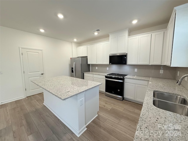 kitchen with sink, a kitchen island, light stone counters, white cabinetry, and stainless steel appliances