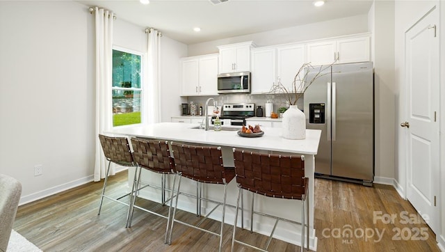 kitchen featuring white cabinets, appliances with stainless steel finishes, tasteful backsplash, sink, and a center island with sink