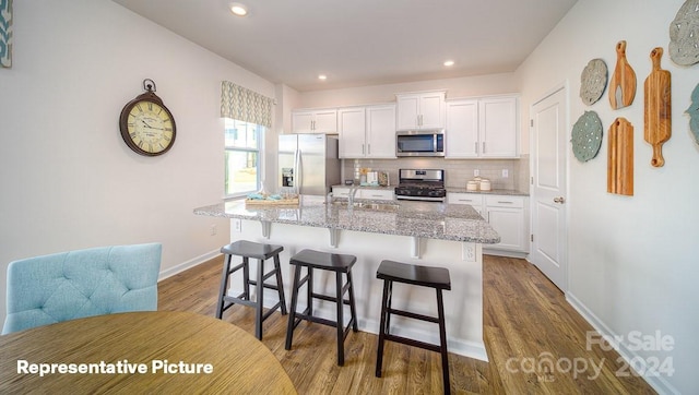 kitchen featuring a breakfast bar area, a center island with sink, wood-type flooring, stainless steel appliances, and white cabinets