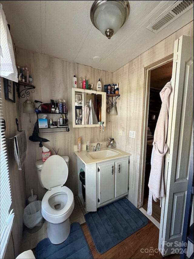 bathroom featuring wood-type flooring, toilet, wooden walls, and vanity