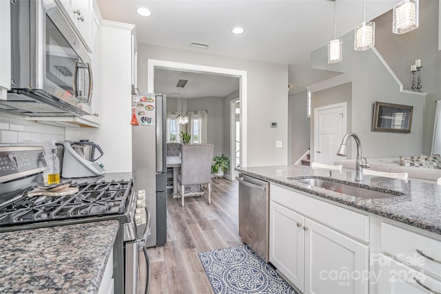 kitchen featuring dark stone countertops, light wood-type flooring, appliances with stainless steel finishes, white cabinetry, and sink