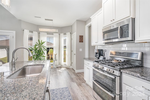 kitchen featuring dark stone countertops, appliances with stainless steel finishes, light hardwood / wood-style floors, white cabinetry, and sink