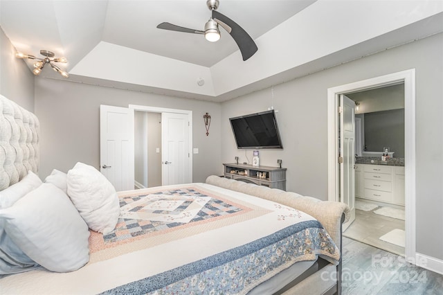 bedroom with ensuite bath, hardwood / wood-style flooring, a tray ceiling, and ceiling fan