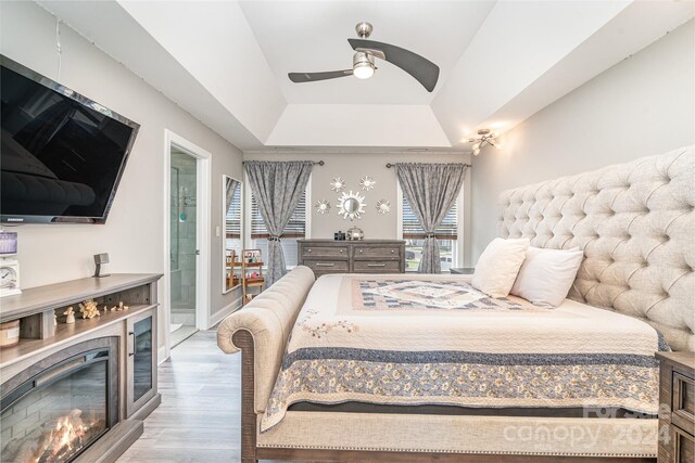 bedroom featuring light wood-type flooring, a tray ceiling, ensuite bathroom, and ceiling fan