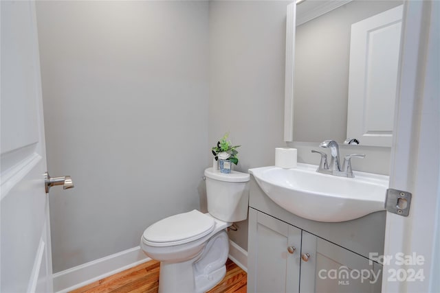 half bath with baseboards, toilet, vanity, and wood finished floors