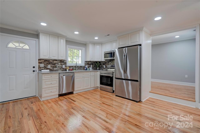kitchen featuring white cabinets, stainless steel appliances, crown molding, and light wood-style floors