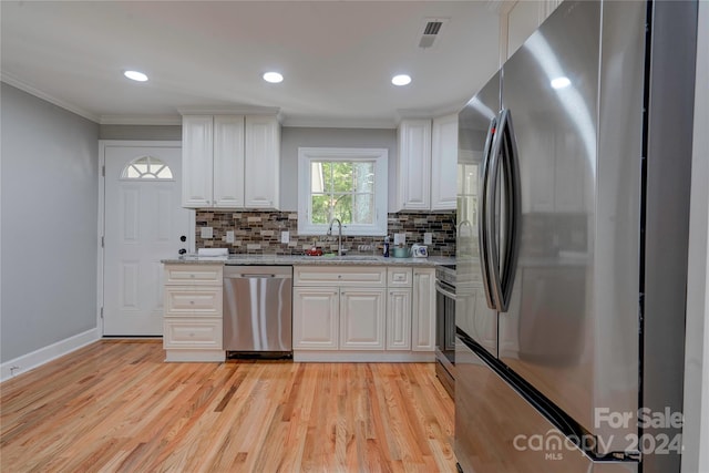 kitchen with white cabinetry, ornamental molding, a sink, light wood-style flooring, and appliances with stainless steel finishes