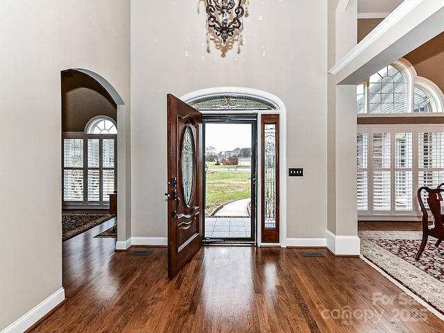 foyer entrance featuring a towering ceiling, dark hardwood / wood-style floors, an inviting chandelier, and a wealth of natural light