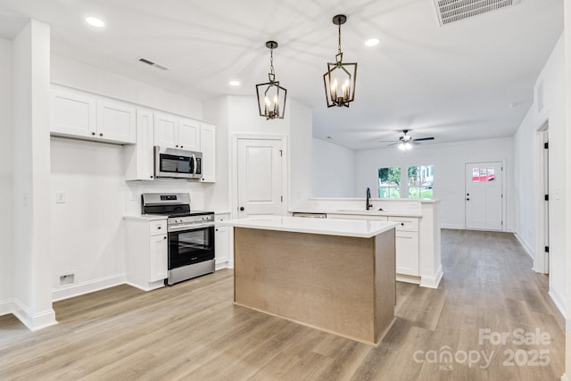 kitchen featuring kitchen peninsula, stainless steel appliances, white cabinets, a kitchen island, and hanging light fixtures