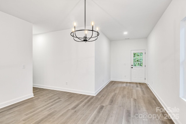 unfurnished dining area with a notable chandelier and light hardwood / wood-style flooring