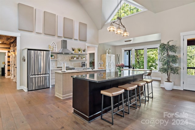 kitchen featuring wall chimney exhaust hood, stainless steel fridge, high vaulted ceiling, and plenty of natural light