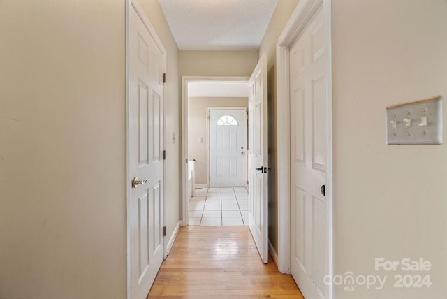 hall with light wood-type flooring and a textured ceiling