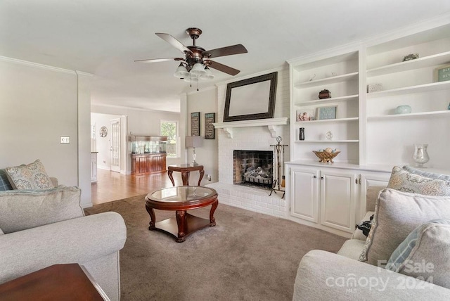 carpeted living room with a fireplace, crown molding, built in shelves, and ceiling fan