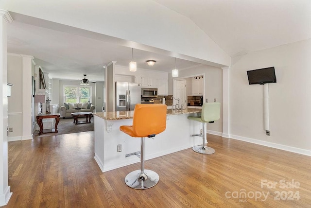 kitchen with a breakfast bar area, hanging light fixtures, stainless steel appliances, white cabinetry, and light wood-type flooring