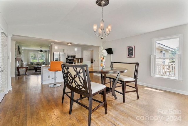 dining space with light wood-type flooring, ceiling fan with notable chandelier, lofted ceiling, and plenty of natural light