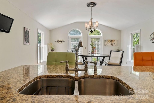 kitchen with lofted ceiling, sink, light stone countertops, and a notable chandelier